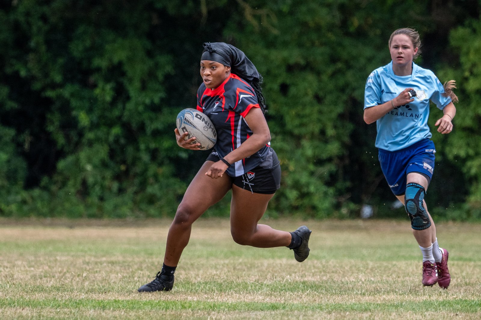 ERA girl in black/red kit running with ball, chased by opponent in light blue